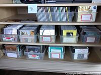 Multiple clear plastic bins on shelves each containing rows of CD jewel cases.