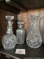 First photo showing two decanters and a large crystal vase on a wooden shelf.