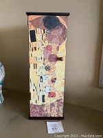 Front view of tall upright jewelry box featuring Klimt's The Kiss artwork covering front panel with a small wooden knob for opening the door.