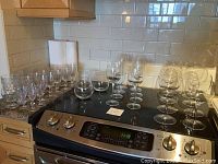 Full view of all crystal and glass stemmed glasses arranged on a stove top, showing different sizes and styles of wine and water glasses.