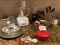 Wide view of the lot showing all items including KitchenAid food processor, Magic Bullet blender, bakeware, cookware, utensils, and measuring spoons.