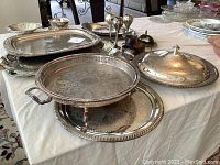 Photo from angle showing multiple silver trays including large rectangular and round trays, and covered dish.