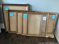 Seven gold picture frames leaning against a wall, showing different sizes with blue measurement sticky notes attached.