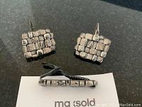 Front view of the two cufflinks showing the raised square block pattern and tie bar in side profile.