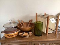 Full view showing all items on display: teak salad bowl and utensils, Pyrex casserole, ceramic bowl, green glass, silver serving dish, and teak magazine holder.