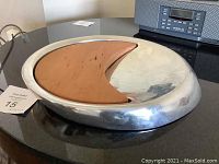 Modernist aluminum cheese board with removable crescent-shaped wood cutting board inside. Surface shows some wear marks and scratches.