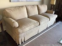 Angled front view showing three seat cushions, rolled arms and pleated skirt