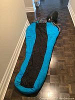 Turquoise and black Moonstone sleeping bag fully unrolled on floor, showing mummy style with hood and black central panel.