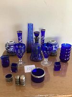 Front view of all lot items arranged on table, showing blue glassware with various shapes and decorative details including salt and pepper shakers