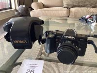 Side view showing Minolta 7000 Maxxum camera body with attached flash and lens with cover on, placed on a glass table.