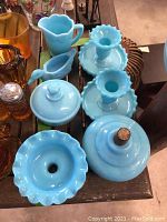 Top view of all 7 blue milk glass items arranged on a table, showing candlesticks, covered sugar, creamer, duck, lamp part, and dish.