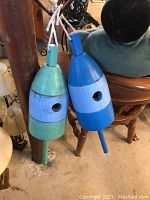 Photo showing two wooden buoy-shaped birdhouses hanging side by side, one painted green and light blue, the other painted shades of blue.