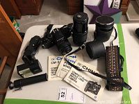 Photo shows Chinon CM-3 camera with two additional lenses, lens hoods, camera strap, and instruction manuals on a surface.