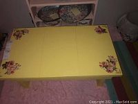 Top-down photo of the yellow wooden coffee table with floral patterns at corners, displaying surface condition and scratches.