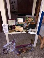 Wide view of collection on small table showing brooch, rings, watches, toy, spoon, cuff links, and boxes.