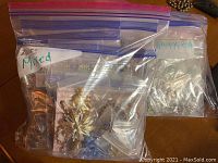 Multiple clear plastic bags containing mixed costume jewelry including pins, bracelets, and necklaces with metal and beaded designs.