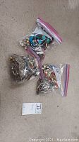 Three zip-lock bags filled with assorted costume jewelry bracelets placed on a floor surface.