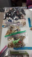 Three clear zip-lock bags filled with assorted costume jewelry including earrings and brooches shown on a table.