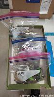 Three resealable plastic bags containing assorted costume jewelry pieces inside a box, viewed from above