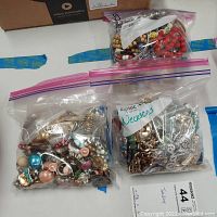 Three ziplock bags filled with assorted costume jewelry including bead necklaces, metallic chains, earrings, and bracelets.