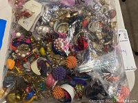 Bag with a large assortment of colorful costume jewelry earrings in various shapes and materials including plastic and metal.