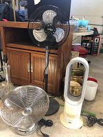 All three fans grouped: Dyson AM04 white bladeless fan with discolored yellowed base, Hunter black pedestal fan, Nantucket Breeze chrome floor fan