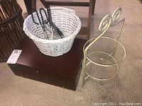 Full lot view with flatware box on wooden chest, white wicker basket with kitchen utensils, and metal plate holder next to them