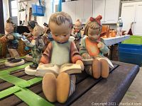 Photo of two Hummel figurines, a boy and a girl reading books, displayed on a wooden surface.