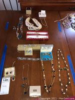 Overview photo of assorted jewelry laid on a table including necklaces, sets of earrings and bracelets, and multi-strand pearl-like necklace.