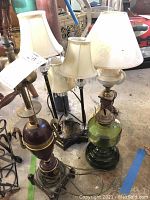 Three table lamps with shades and one oil lamp without chimney shown together in garage space.