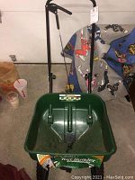 Full view of the green Scotts Turf Builder plastic spreader with black metal handle and lever control, showing the overall condition and size.