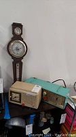 Photo showing all three main items together: Springfield wooden barometer on wall, General Electric cream radio on the left, and blue-green Motorola radio on the right.