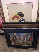 Framed Japanese Tea Towel with fans and kimono fabric artwork partially visible behind framed Times Square print and another wooden framed painting.