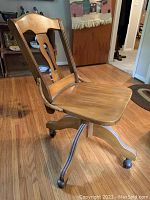 Side angle showing the profile, curved backrest, shaped wood seat, and wheel casters on bent wooden legs.