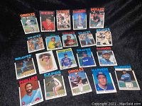 Collection of 1984 Topps baseball cards laid out on black fabric, showing multiple players from teams like Orioles, Reds, Braves, Phillies, Rangers, Expos, Mariners, Astros, and Indians.