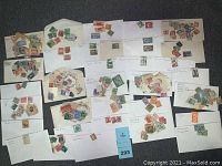 Image of multiple white envelopes with assorted foreign stamps, both loose and attached, spread out on a surface showing variety and quantity of stamps in lot.