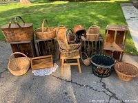 Overview of lot showing multiple farmhouse baskets, wooden crates, wooden step stool, and hand painted decor bucket outdoors on paved surface with grass background.