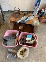 Lot of outdoor ice fishing equipment arranged on a wooden surface and bins on the floor, showing molds and miscellaneous materials.