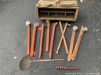 Wide view of the ice fishing gear laid out on asphalt, showing tip ups, scoop, and gaff hook with carrying case behind them.