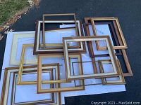 Group of 14 large size art frames stacked outdoors on ground showing variety of wood finishes and gold frames with some missing glass.
