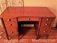 Front view of mid century modern wooden desk showing seven drawers, central curved ergonomic cutout, brass handles, and finished wooden surface.