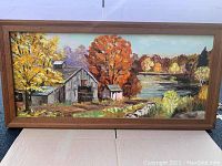 Framed oil painting showing an autumn landscape with barn, smaller buildings, and a lake in the background. Vivid fall colors and rough brushwork visible.