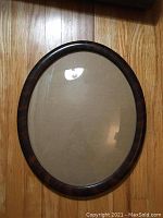 Full view of the antique oval wooden frame with bubble glass on a wooden floor, showing the overall shape and condition.