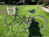Side view of green Raleigh C-30 bicycle with white basket on front, black seat, and tires on grass.