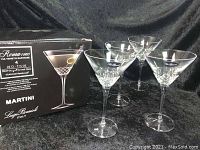 Photo showing four clear crystal martini glasses displayed in front of original product box featuring brand and product details.