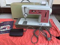 Full view of the Singer Touch & Sew Model 626 sewing machine with foot pedal and carrying case behind it, placed on a red cloth.