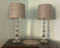Pair of acrylic lamps with stacked ball bases on a wooden surface against a pale wall.