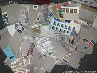 Stacked and scattered groups of stamps in transparent plastic sleeves and original packaging on a dark carpet.