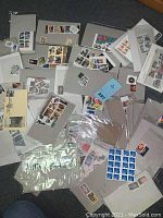 Photo showing 53 groups of various stamps in original packaging and loose on a dark surface