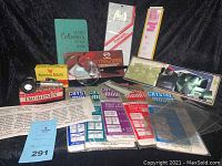 Full group of stamp collecting supplies laid out on dark cloth background, shows magnifier, watermark detector, mounts, stock book, and reference sheets